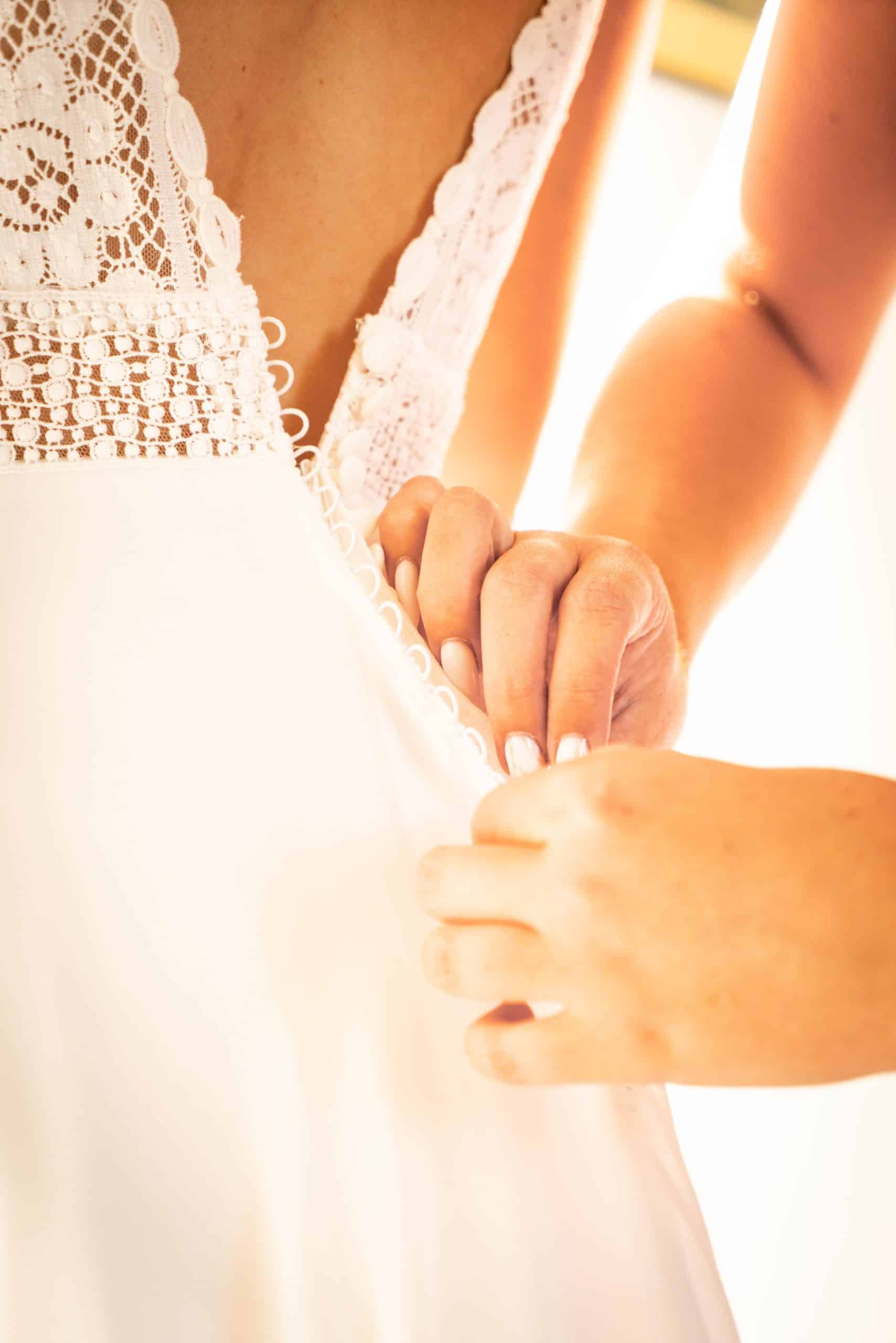 La témoin de la mariée ferme la robe. ©Maxime Bonneau, Nautile Photographie 2023.